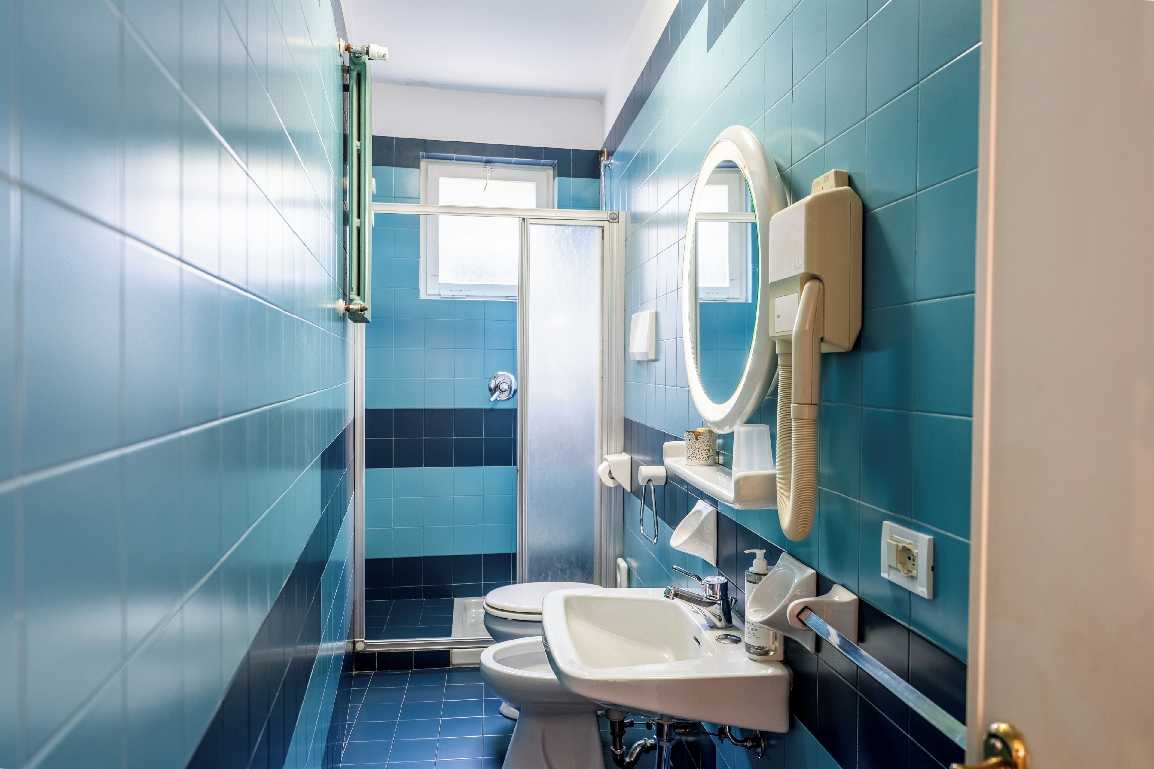 A bathroom with blue tiles, a shower, a toilet, a sink, and a mirror.