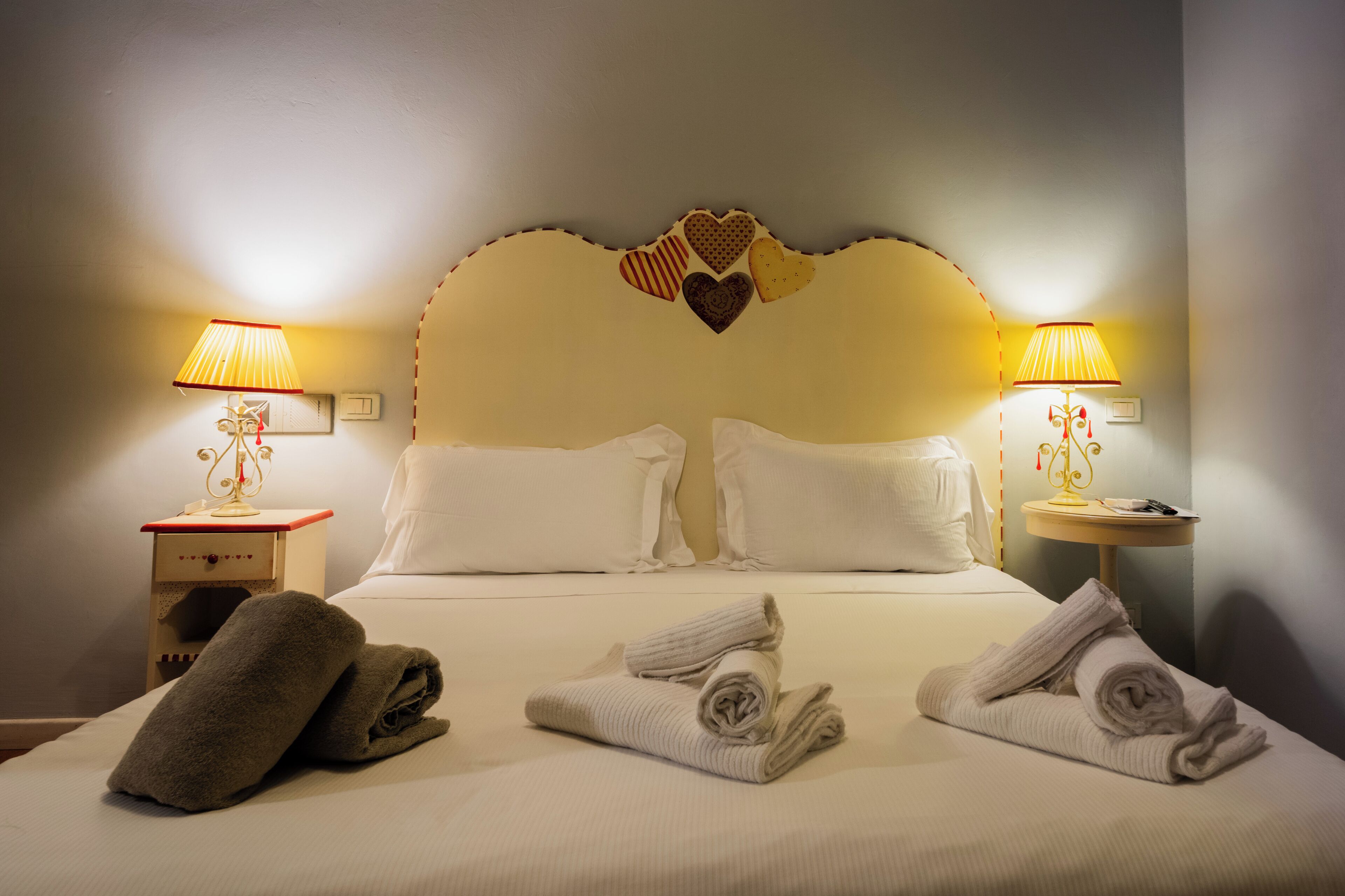 A neatly made bed with white linens, two bedside lamps, and towels on the bed.