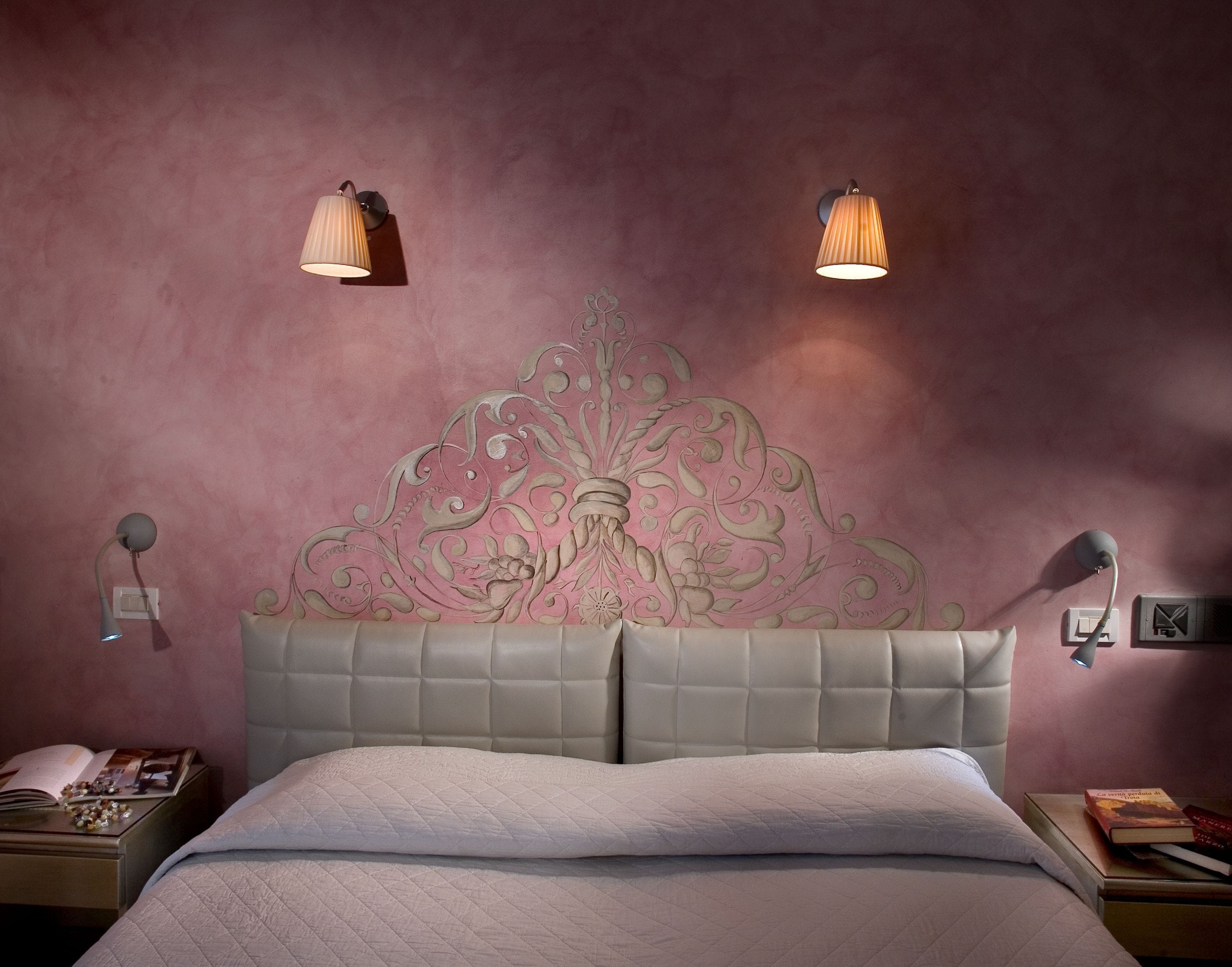 A bedroom with a tufted headboard, two wall-mounted lamps, and a bedside table with a book and decorative items.