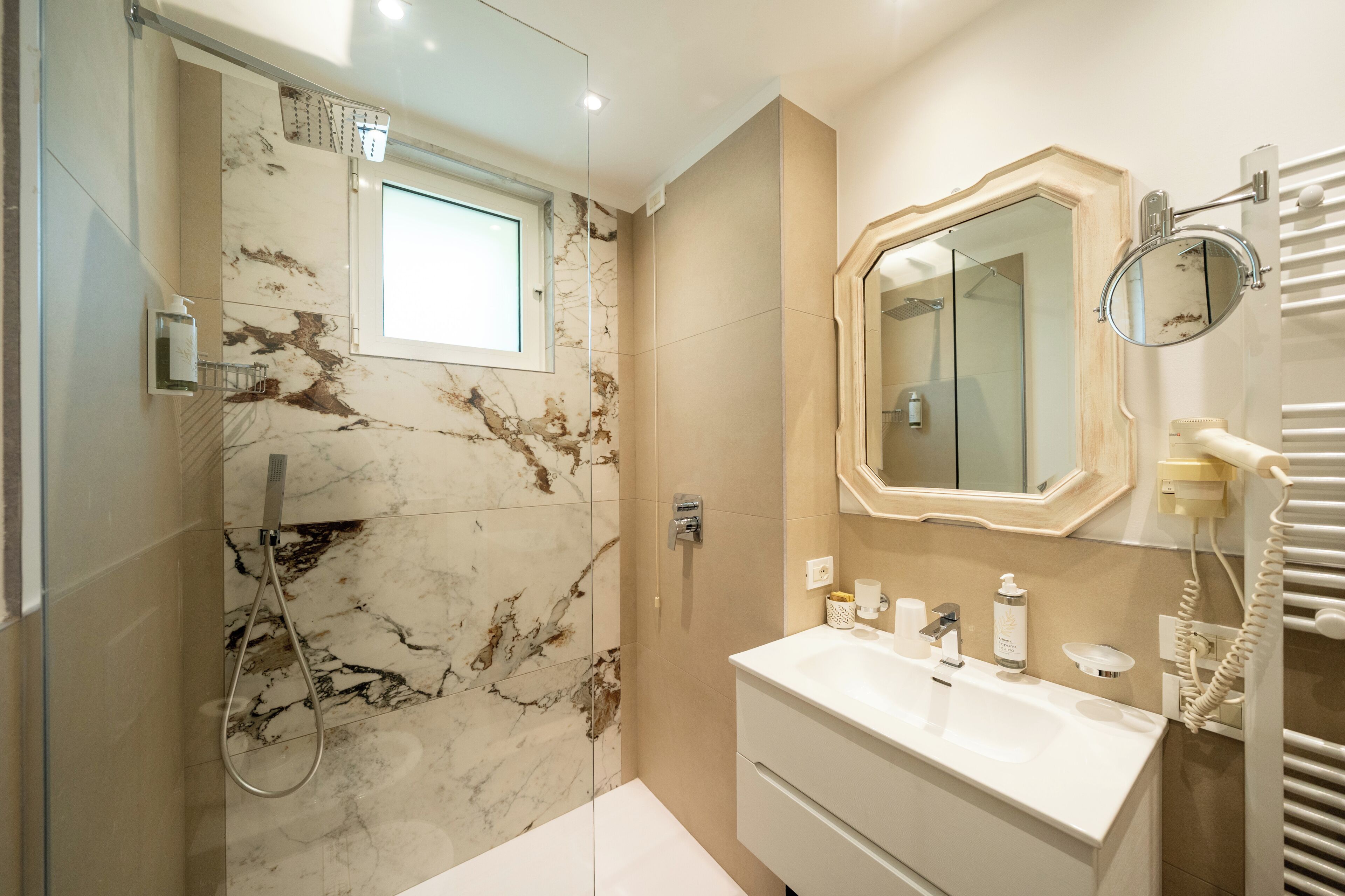 A bathroom with a marble wall, a sink, a mirror, and a towel rack.