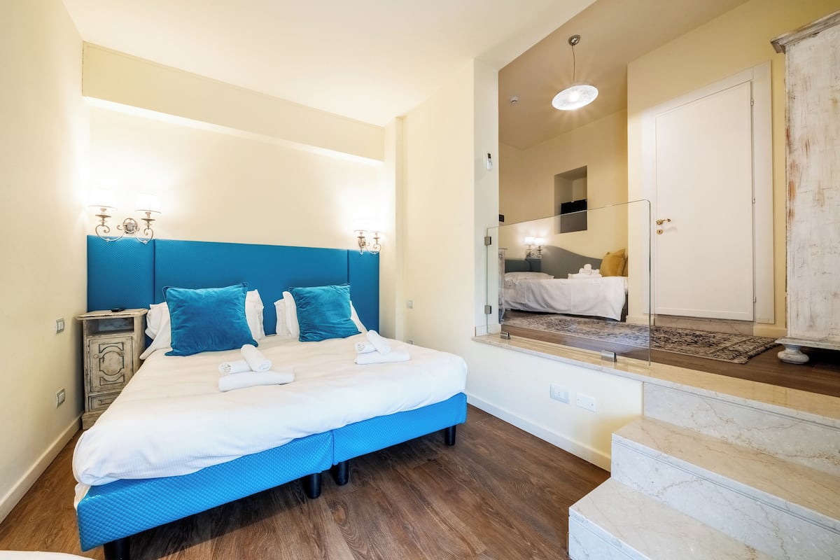 A bedroom with a bed, a nightstand, a mirror, a wardrobe, and a staircase.