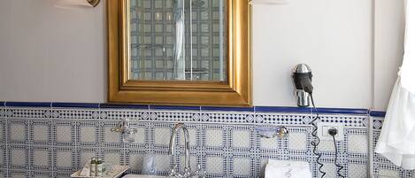 A bathroom with a white sink, a mirror with a gold frame, and blue patterned tiles.