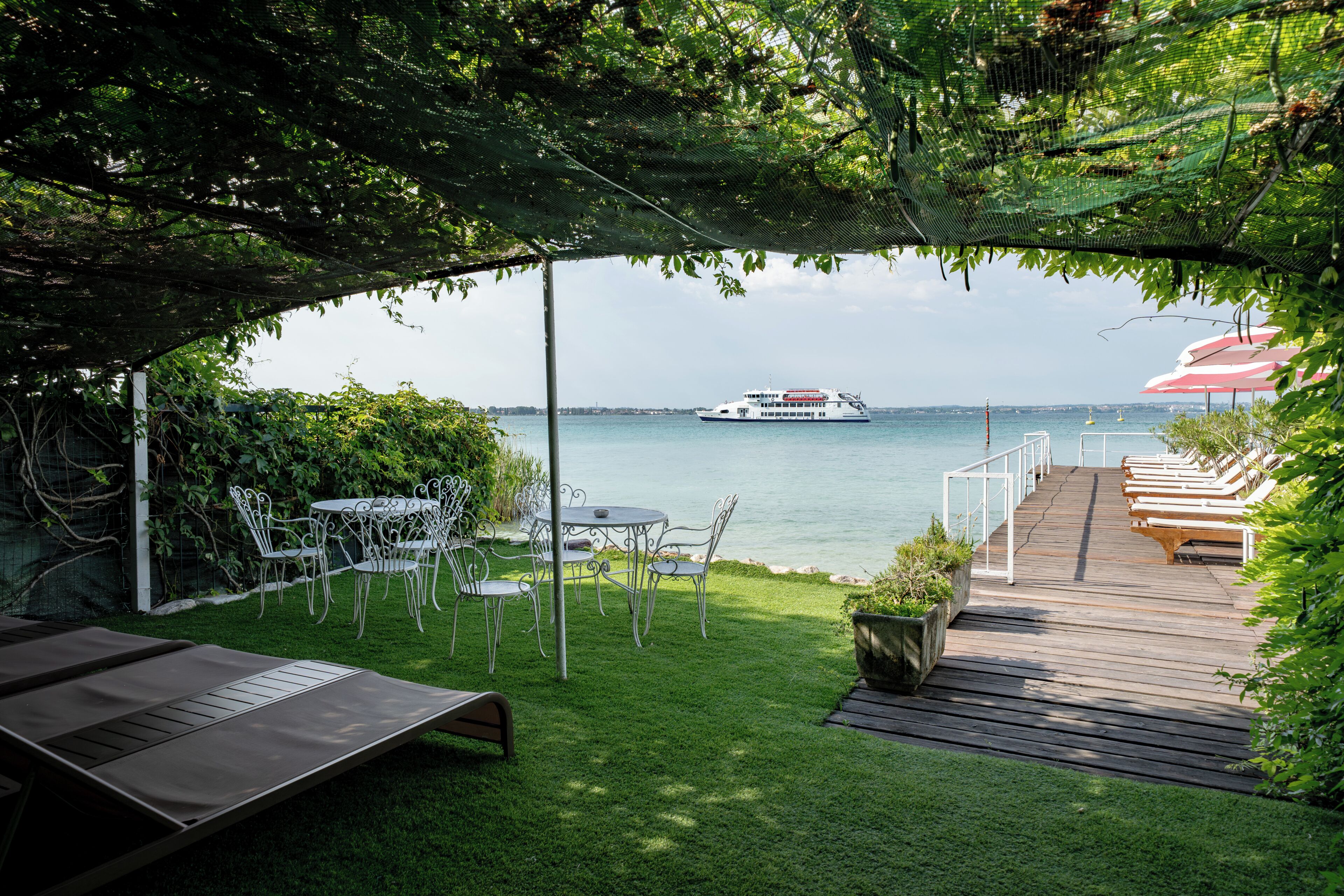 A patio with a view of the water, a boat, and a deck with lounge chairs.