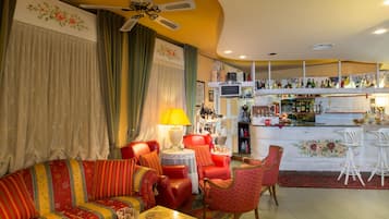 Un salon comprenant un canapé, des fauteuils, une table et un coin bar avec des étagères remplies de bouteilles.