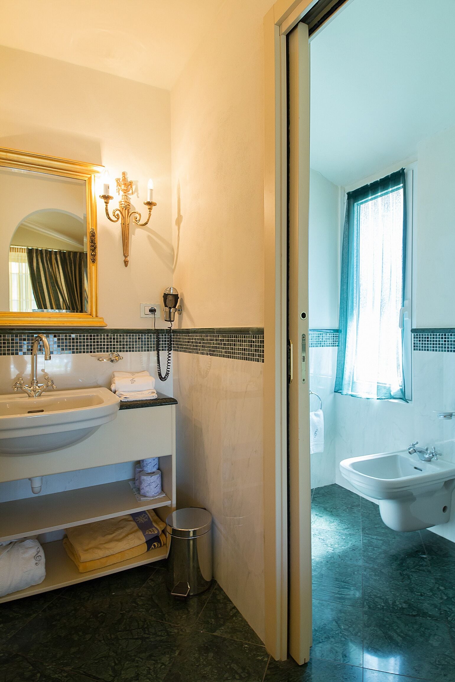 A bathroom with a sink, mirror, and vanity. There is a trash can and a shower visible.