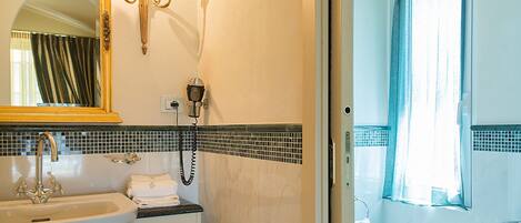 A bathroom with a sink, mirror, and vanity. There is a trash can and a shower visible.