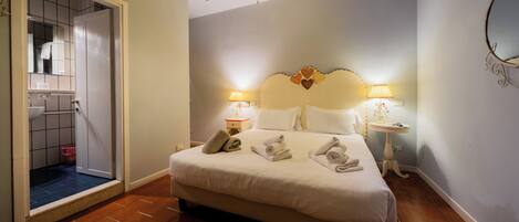 A hotel room with a bed, bedside lamps, a chandelier, and a bathroom visible through an open door.