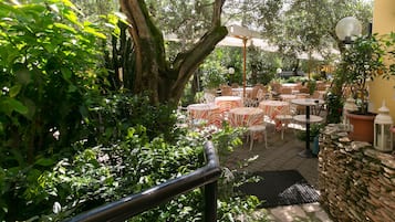An outdoor patio area with tables and chairs, surrounded by lush greenery and trees.