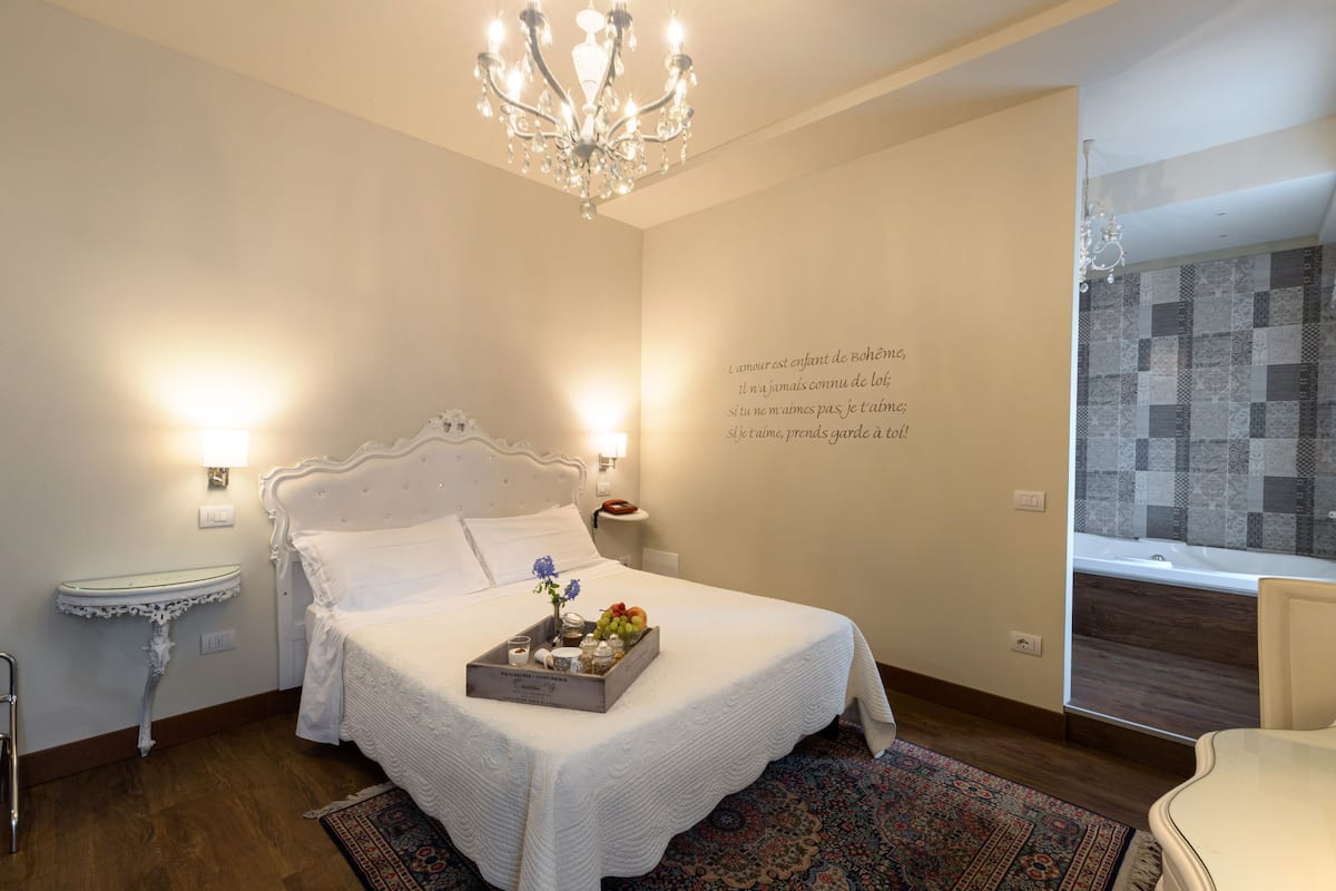 A neatly arranged bedroom with a large bed, bedside tables, a chandelier, and a decorative wall with a quote.