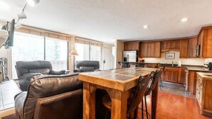 Un vaste espace de vie comprenant un coin repas avec une table en bois, des canapés en cuir et une cuisine dotée de meubles en bois.