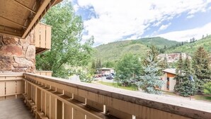 Un balcon doté d’un mur en pierre et d’une balustrade en bois, offrant une vue sur une région montagneuse parsemée d’arbres et de bâtiments.