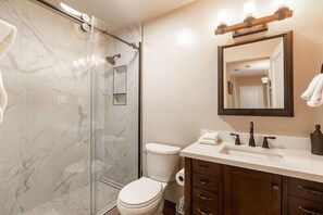 Une salle de bain avec une douche à parois de verre, des toilettes, un lavabo avec un miroir au-dessus et des meubles en bois.