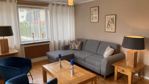 Una sala de estar moderna con un sofá gris, sillones azules, una mesa de centro de madera y dos mesitas de noche con lámparas.