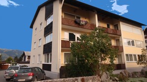 Un edificio de varios pisos con balcones, un muro de piedra y coches estacionados.