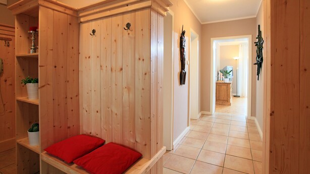 Un interior de madera con un banco, estanterías con plantas y un pasillo que lleva a una zona de cocina.
