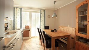 Una cocina con una mesa de madera, sillas y un banco. Hay un lavamanos, estufa y armarios.