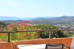 A balcony with a view of a coastal landscape, including hills and a body of water.