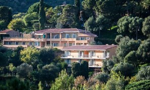 A multi-story building with balconies, surrounded by dense greenery and trees.