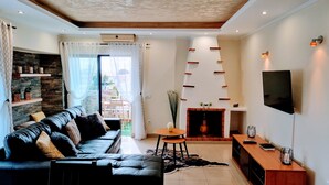 A modern living room with a black leather sofa, a fireplace, a TV mounted on the wall, and a stone accent wall. - OURASOL 2 Bedroom Apartment in Santa Eulalia, Albufeira Centre  (Albufeira)