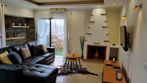 A modern living room with a black leather sofa, a fireplace, a mounted TV, and a stone wall. - OURASOL 2 Bedroom Apartment in Santa Eulalia, Albufeira Centre  (Albufeira)