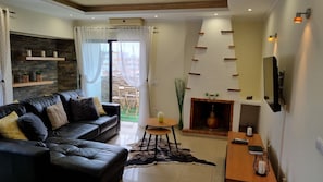 A modern living room with a black leather sofa, a fireplace, a mounted TV, and a stone wall.