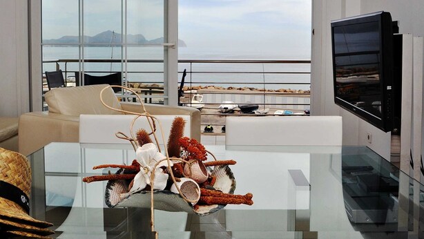 A modern living room with a glass coffee table, a sofa, and a television. The room has large windows offering a view of the sea and mountains. - Minimal, sea views apartment first line (Santa Margalida - Can Picafort/Son Serra Marina)