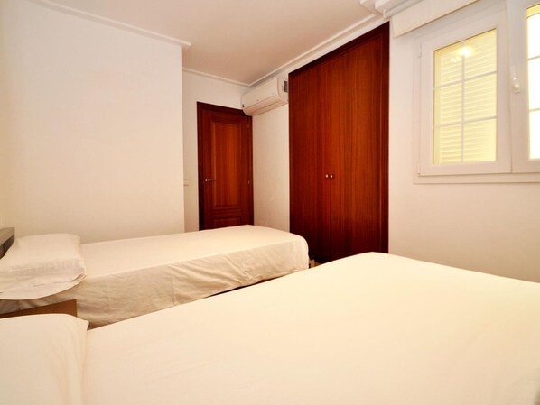 A bedroom with two single beds, a wooden wardrobe, and a window with blinds. - Minimal, sea views apartment first line (Santa Margalida - Can Picafort/Son Serra Marina)