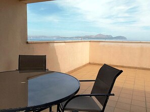 A balcony with a round table and two chairs, a view of the sea and mountains in the background.