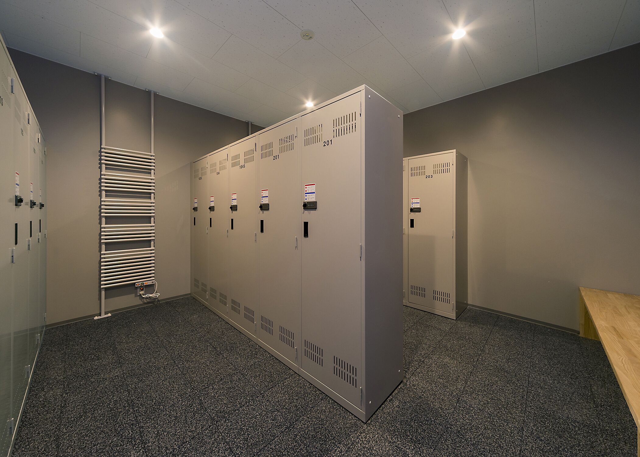 A row of lockers with numbers, a radiator, and a door with a lock.