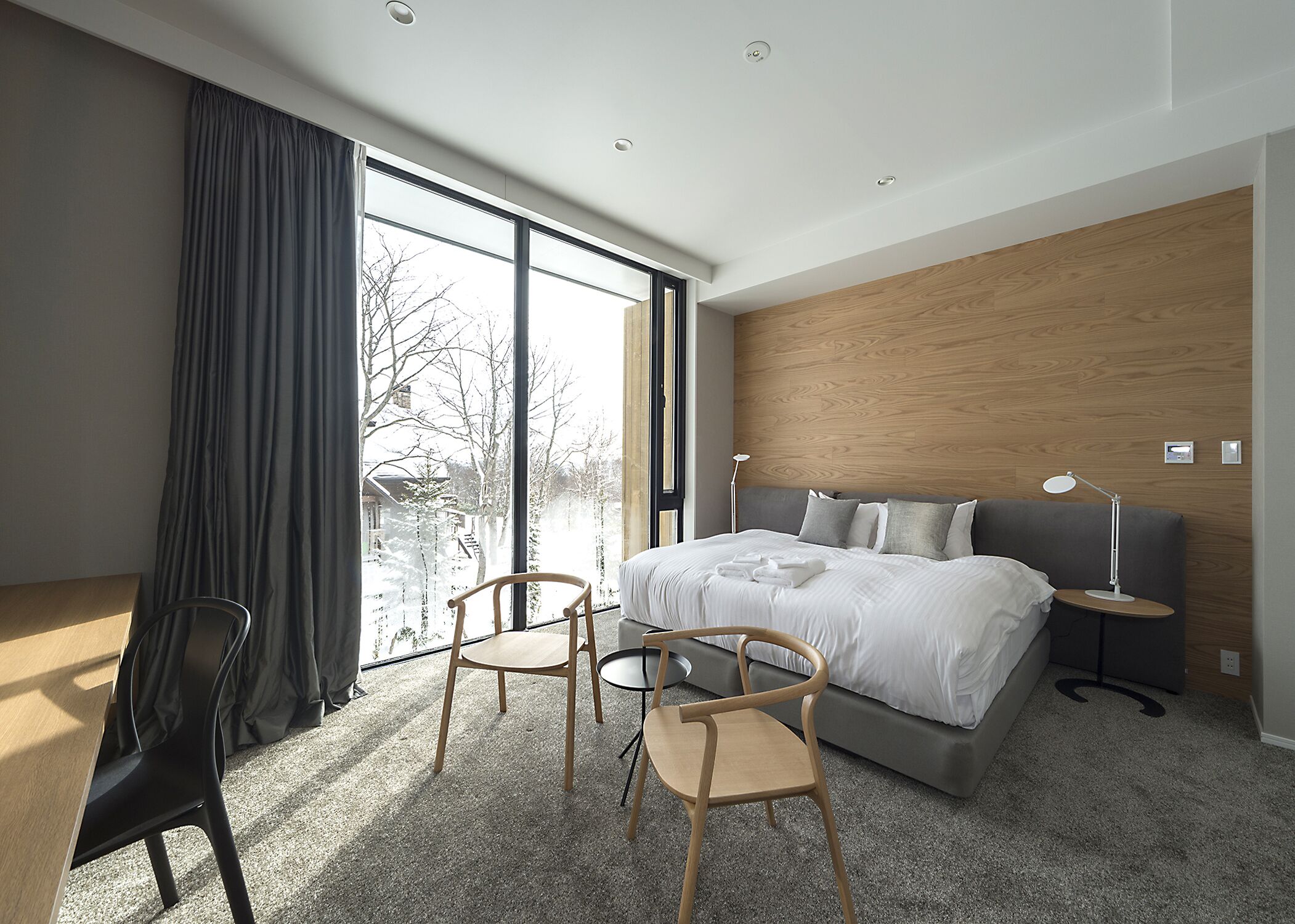 Une chambre d’hôtel moderne avec un grand lit, deux fauteuils, un bureau et une vue sur l’extérieur.