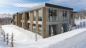 Un edificio moderno con grandes ventanales y fachada de concreto, rodeado de nieve y árboles.
