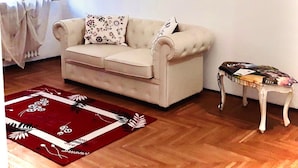 A living room with a beige sofa, a red patterned rug, a small side table, and a wall clock.