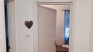 A room with a wooden floor, a white door, a heart-shaped welcome sign, and a towel on a bench.