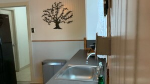 A kitchen with a stainless steel sink, a refrigerator, and a decorative tree wall art. - SHOTGUN HOUSE (Angleton)