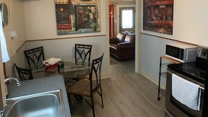 A compact kitchen with a dining table, chairs, a microwave, and an oven. There is a painting on the wall depicting a street scene. - SHOTGUN HOUSE (Angleton)