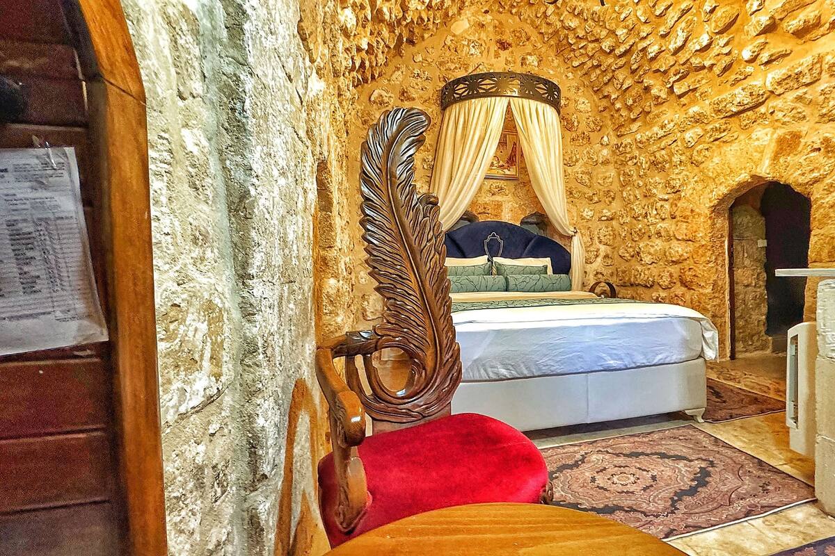 A room with a stone wall, a bed with a canopy, a wooden chair, and a small Christmas tree.