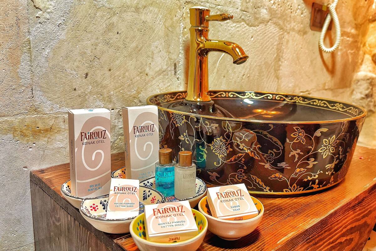 A bathroom vanity with a gold faucet, a decorative bowl sink, and various personal care products including soap and cotton buds.