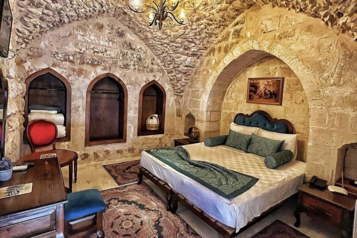 A bedroom with a stone ceiling, a bed with green and white bedding, a chandelier, and a red chair.