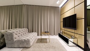 Een moderne woonkamer met een gestoffeerde bank, een flatscreen televisie aan de muur en een groot raam met gordijnen.