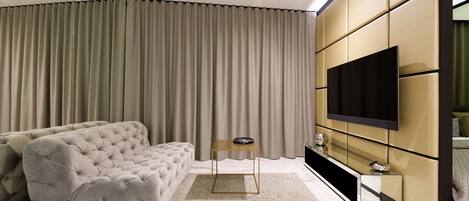 A modern living room with a tufted sofa, a flat-screen TV mounted on a wall, and a large window with curtains.