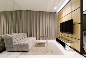 A modern living room with a tufted sofa, a flat-screen TV mounted on a wall, and a large window with curtains.