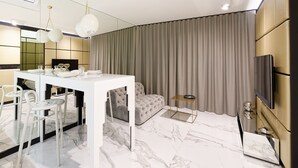 Een moderne woonkamer met een witte eettafel, een grijze bank en een aan de muur bevestigde televisie.