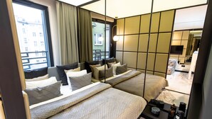 Een moderne hotelkamer met twee bedden, een groot raam met gordijnen, uitzicht op de stad en een klein tafeltje met kaarsen.