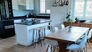 Eine moderne Küche mit weißen Schränken, einem schwarzen Kühlschrank und einem Holzespeisetisch mit weißen Stühlen.