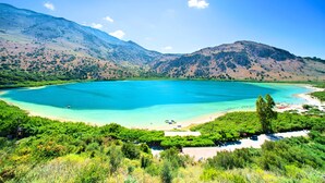 A coastal landscape with a large turquoise lake, surrounded by green hills and a clear sky.