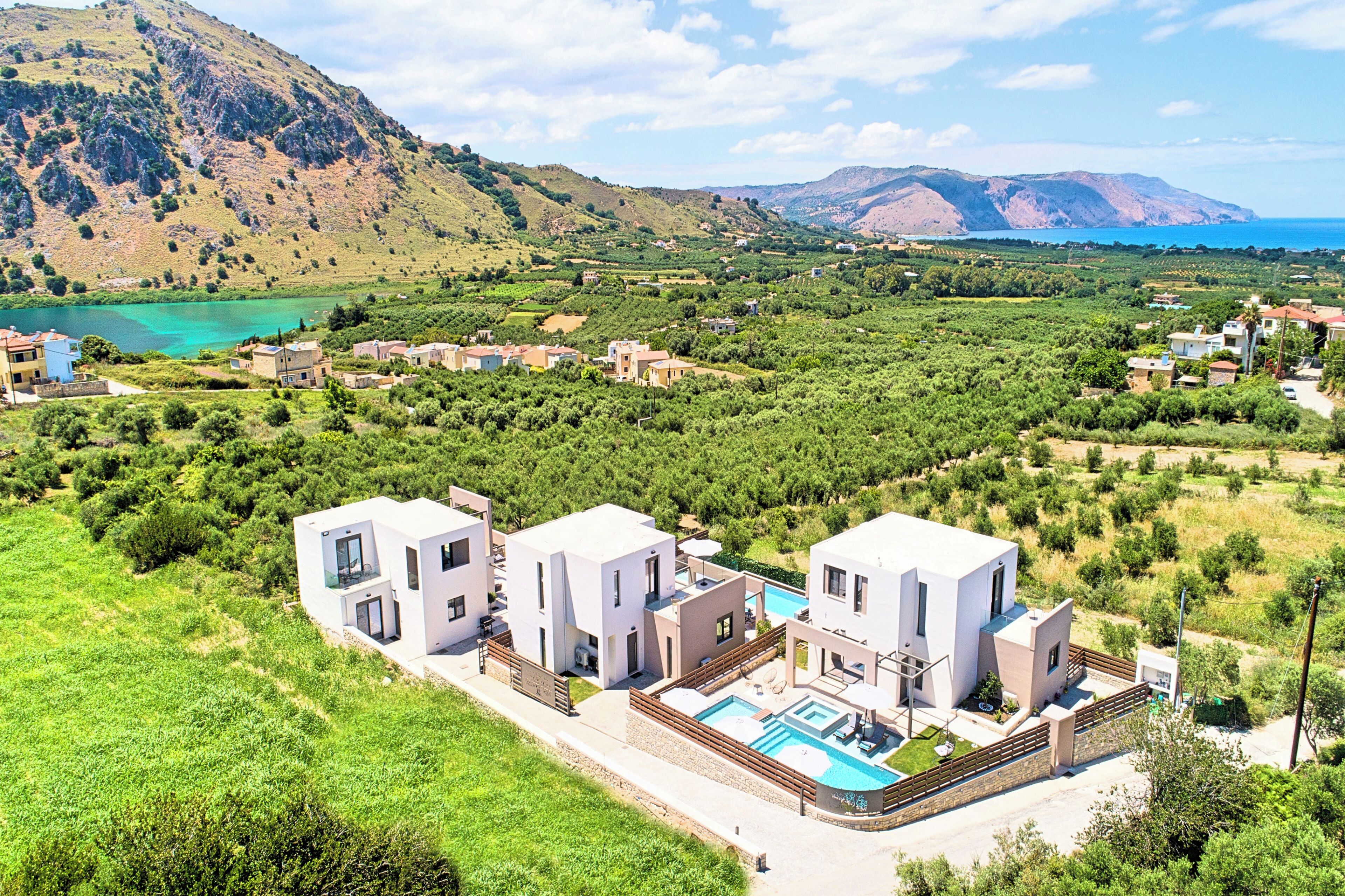 A modern villa with a swimming pool, surrounded by lush greenery and mountains.