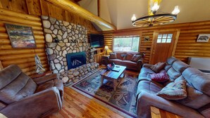 Ein rustikales Blockhaus-Interieur mit Kamin aus Stein, Ledersofas, einem Holztisch und einem an der Wand befestigten Fernseher.