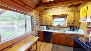 Eine Küchenzeile im Blockhausstil mit Holzschränken, einer Mikrowelle, einem Spülbecken und einem Fenster mit Blick auf einen Garten.
