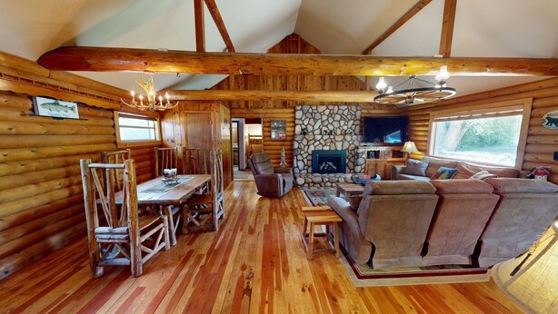 Ein Holzblockhaus-Interieur mit Essbereich, Kamin, einer Couch und einem Fernseher.