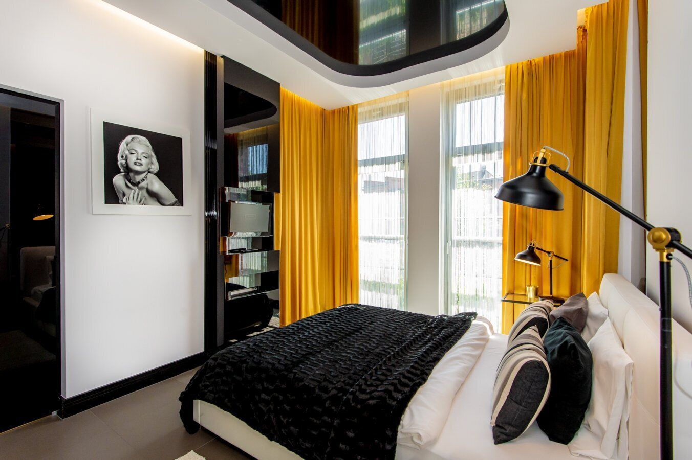 A modern bedroom with a bed, a bookshelf, a desk, and a large window with curtains.